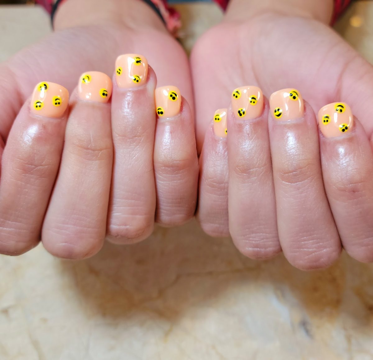 Short peach nails with tiny smiley faces